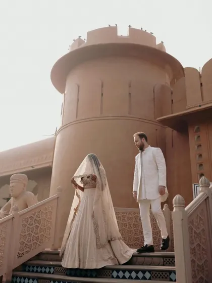 Priyanka and Luke on the steps of a fort-like structure at the Oberoi Rajvilas. The bride's veil adds a touch of mystery and elegance to this post-wedding editorial shot.