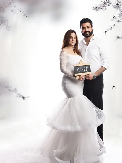 A lovely gender reveal photo. The couple stands together in a dreamy, light-filled setting, holding a sign that says 'It's a Girl', sharing their happy news.