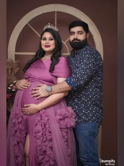A regal maternity portrait. The mom to be wears a crown and a beautiful purple gown, looking every bit the queen she is.
