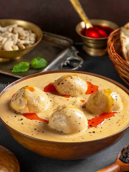 Malai Kofta curry with soft dumplings in a rich, creamy white gravy, garnished with a hint of red oil.