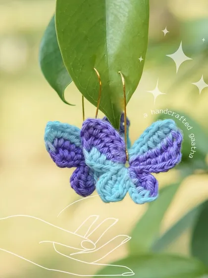 A close-up of the blue and purple 'Titli' earrings. The 100% cotton yarn makes them incredibly lightweight and comfortable.
