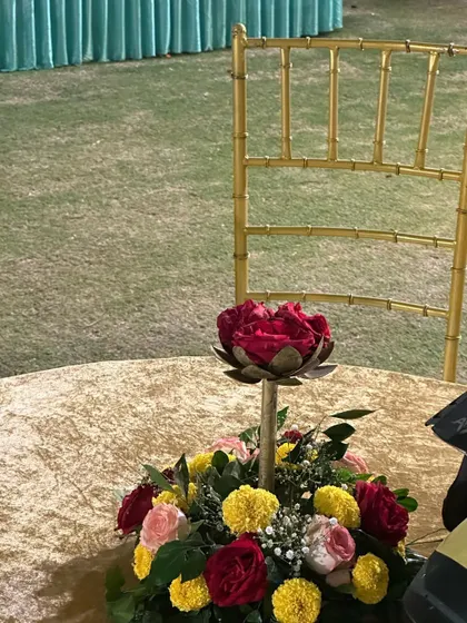 A close-up of a table centerpiece at the Haldi event. The arrangement includes a mix of yellow marigolds and red roses, tying into the overall colorful theme.