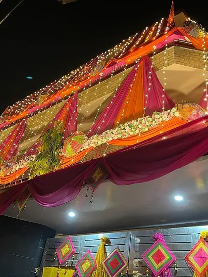 A full view of the brightly decorated wedding house at night. The combination of colorful drapes, lights, and traditional hangings creates a spectacular look.