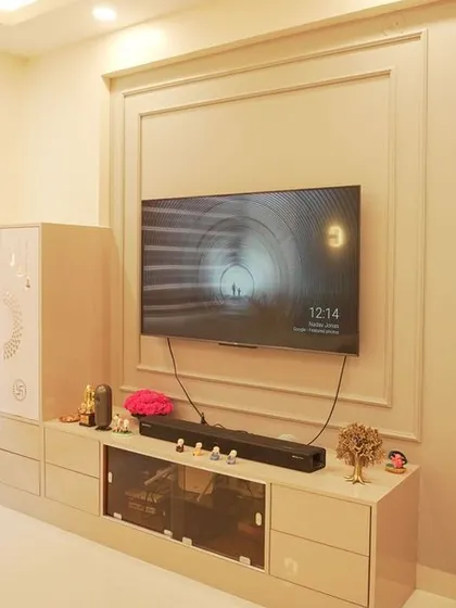 A compact living area in a 1BHK apartment, featuring a TV unit with an integrated pooja cabinet. The wall is decorated with classic beading for a touch of elegance.