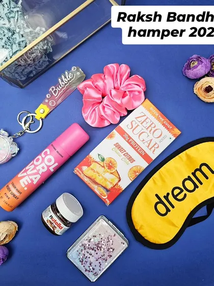 A flat lay of our sister special Rakhi hamper. This collection includes a sleep mask, body spray, a keychain, a scrunchie, and some sweet treats, all curated to pamper her.