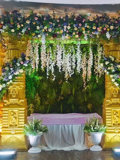 This temple-themed stage combines golden pillars with a lush green backdrop and hanging white flowers, creating a rich and divine setting for any ceremony.