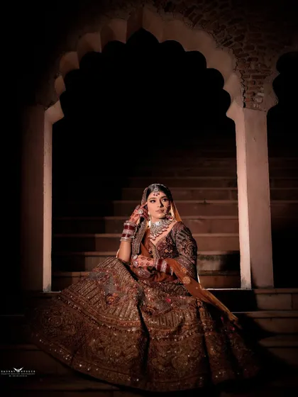 A contemplative portrait of the bride seated on heritage steps. The dramatic lighting focuses on her, creating a quiet and intimate moment amidst the grandeur.