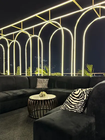 A modern and chic lounge area with black velvet sofas and zebra-print cushions, set against a backdrop of illuminated arches overlooking a city skyline.