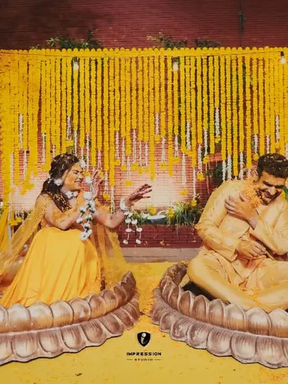 A playful moment during the haldi ceremony, with the couple seated in large lotus-shaped pots, laughing as they are covered in turmeric.