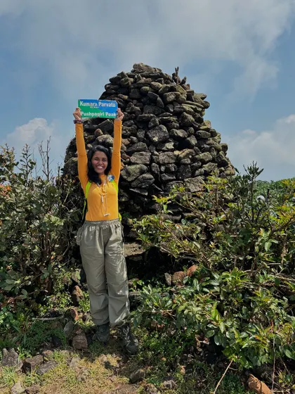 A trekker proudly holds up the Kumara Parvatha sign at the summit. It's a badge of honor for completing this challenging climb.