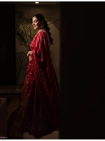 A stunning portrait of the bride, Aashrita, in her red Mehendi outfit. The dramatic lighting and her elegant pose create a powerful and artistic image.