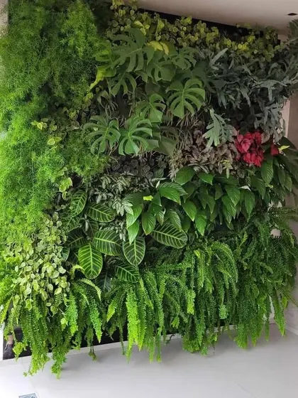A dense and lush artificial green wall installed indoors. This floor-to-ceiling installation uses a variety of large-leaf and trailing plants to create a dramatic, jungle-like effect.