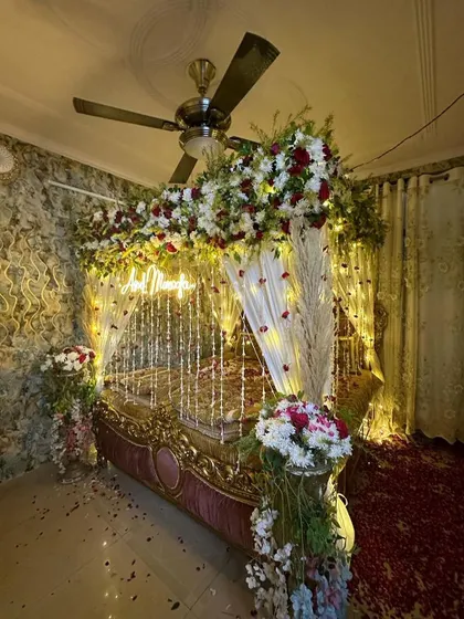 An elegant wedding night setup with a bed decorated with a floral canopy and a custom neon sign. The room is filled with the soft glow of fairy lights.