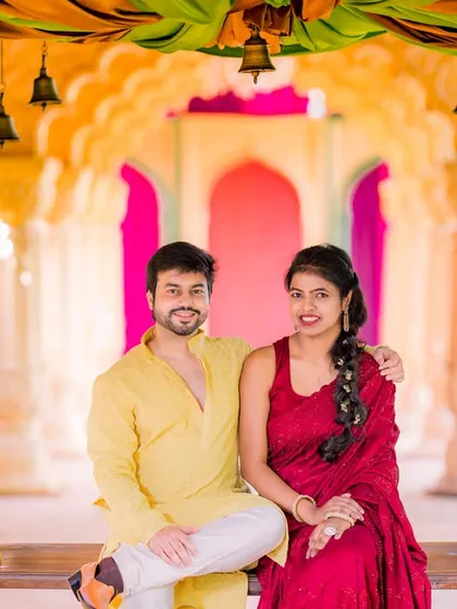 A happy couple poses on a decorated swing. The vibrant colors of the setting and their traditional attire create a joyful and festive atmosphere.