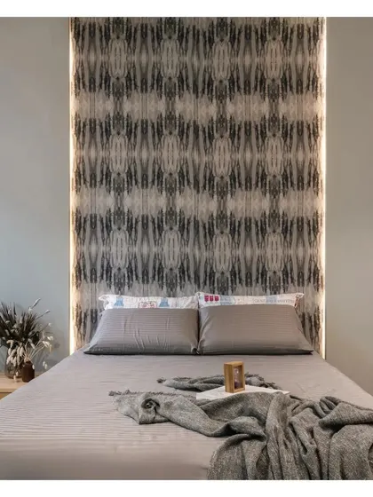 A direct shot of the bed and the feature wall. The symmetrical, abstract pattern of the wallpaper adds a bold graphic element to the otherwise minimalist and serene bedroom design.