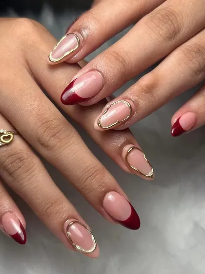 A sophisticated design with a deep red French tip and a gold chrome outline on a nude base. This look is modern, chic, and elegant.