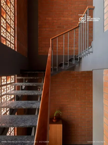 This perspective of the staircase highlights the interplay between the solid brick walls and the perforated jali screen, a key element of the home's bioclimatic design.