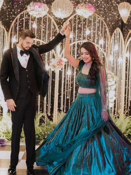 A beautiful couple dancing at their sangeet, set against a stunning backdrop of sparkling light strings and floral arches.