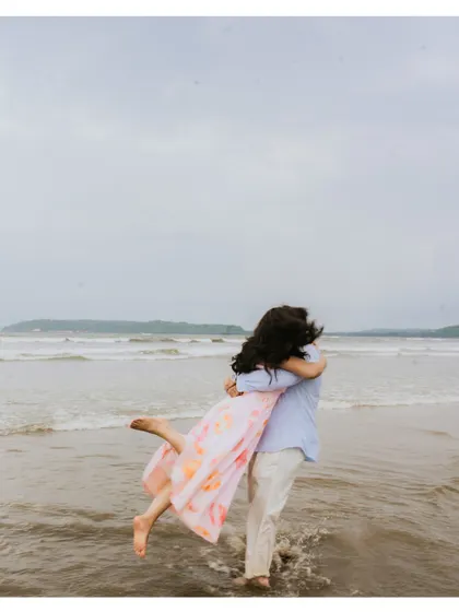 A playful and romantic moment from a beach pre-wedding shoot, with the groom lifting his bride in the shallow water.