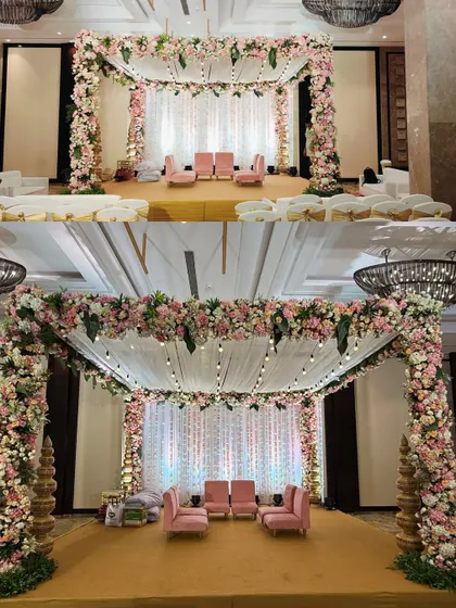 This indoor mandap showcases a beautiful blend of pink and white florals with lush greenery. The draped fabric ceiling with hanging bulbs adds a warm, intimate glow, perfect for an elegant hotel ballroom wedding.