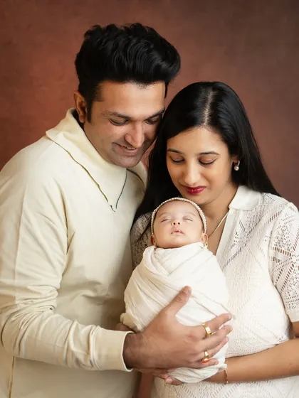 A beautiful portrait of new parents admiring their baby. The coordinated cream outfits create a soft and cohesive look.