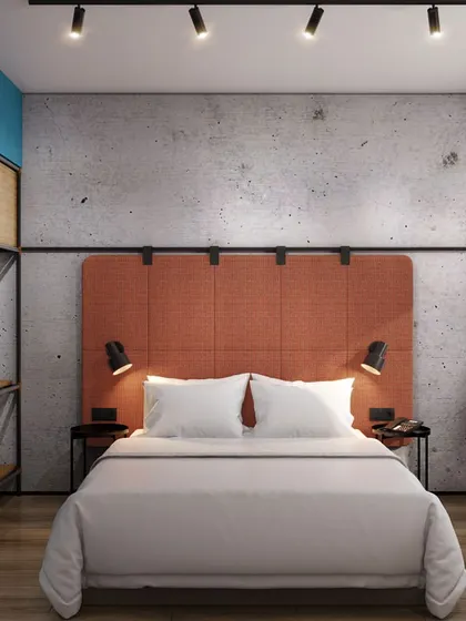 A hotel room with an industrial-chic aesthetic, featuring a concrete accent wall, exposed metal shelving, and pops of color in the furniture.