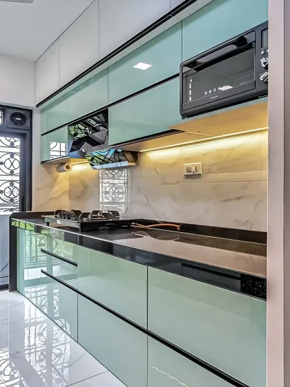 A sleek, modern kitchen with handleless, high-gloss mint green cabinets. The black countertop and integrated appliances create a sharp, contemporary look, while under-cabinet lighting adds a touch of sophistication.