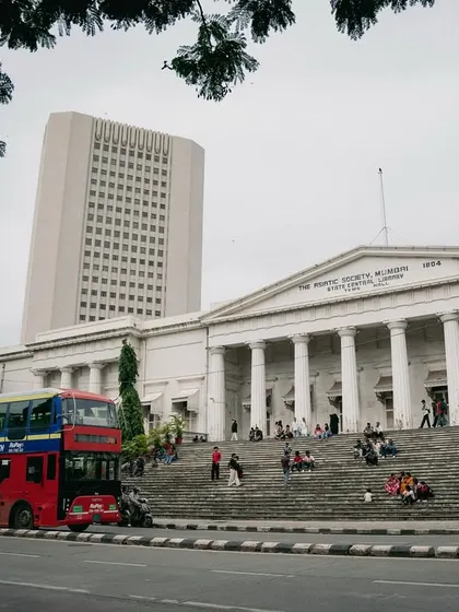 A series of photographs capturing the architectural memory of old Bombay. These images feature landmarks like the Rajabai Clock Tower, the Asiatic Society Library, and other colonial-era structures, often framed by trees.