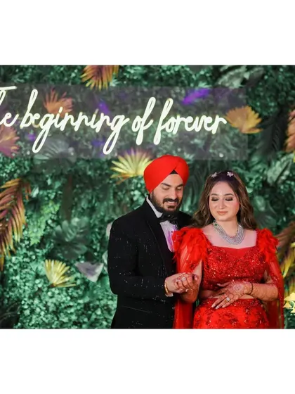 A photo of the couple at their engagement, framed by a neon sign and lush greenery.