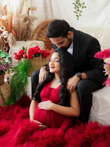A tender moment captured in a beautifully styled setting. The dad-to-be gently kisses his partner's forehead as she cradles her baby bump.