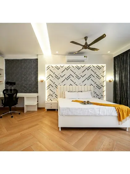 A bedroom that combines crisp white bedding with a bold, geometric accent wall. The herringbone wood flooring adds warmth and texture, while the integrated desk and shelving create a functional and stylish workspace.