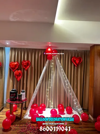 For a cozy and cute surprise, I can set up an indoor canopy tent. This romantic corner is decorated with sheer white fabric, fairy lights, red balloons, and scattered rose petals, creating a perfect little hideaway for a special evening.