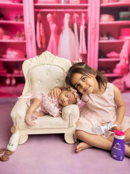 A new big sister gently cuddles her newborn sibling in a whimsical, pink-themed princess closet setup.