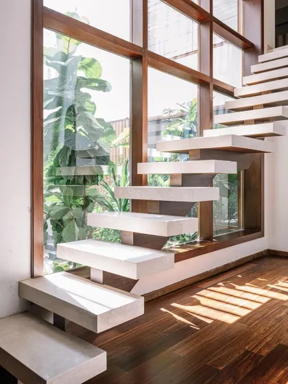 This floating staircase is a feat of minimalist design. The solid stone steps appear to hover against the large window, creating a feeling of lightness. The design allows sunlight to pass through, casting beautiful shadows on the wooden floor.