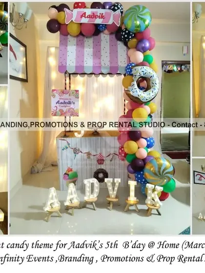 A simple and elegant mini candy cart setup for a 5th birthday at home. This charming decor includes a candy-striped awning, a colorful balloon garland, and a donut prop, creating a sweet corner for the celebration.