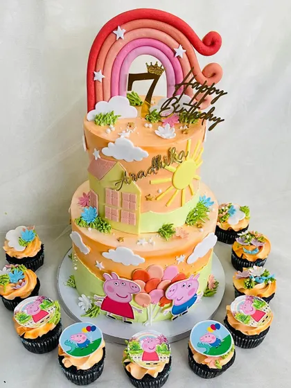 A sunny Peppa Pig themed cake for a 7th birthday celebration. This two-tier cake is decorated with a house, sun, and a rainbow, surrounded by cupcakes featuring the beloved characters.