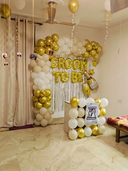 A "Groom to Be" party with a personal touch. This setup includes a gold and white balloon arch and photos of the groom hanging from the ceiling.