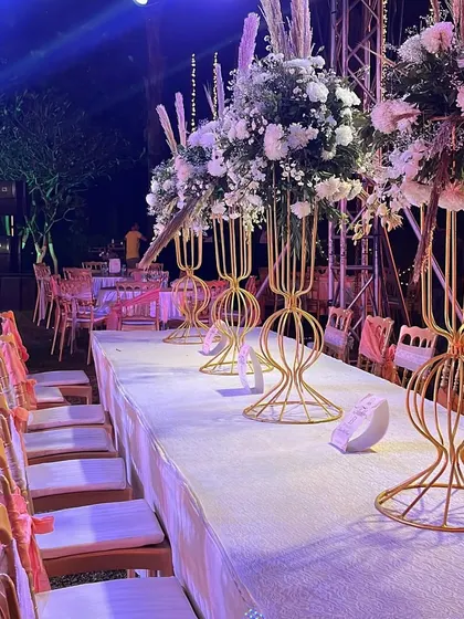Elegant dining tables for an outdoor reception. Long tables are decorated with tall floral centerpieces, creating a sophisticated and communal dining experience under the stars.