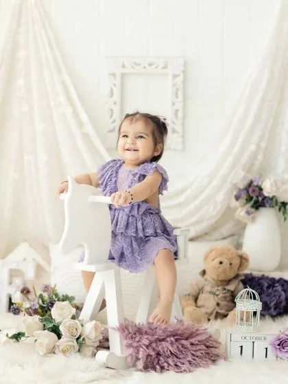 A happy girl on her rocking horse. This first birthday setup in shades of purple with lace and floral details is perfect for a sweet and dreamy photoshoot.