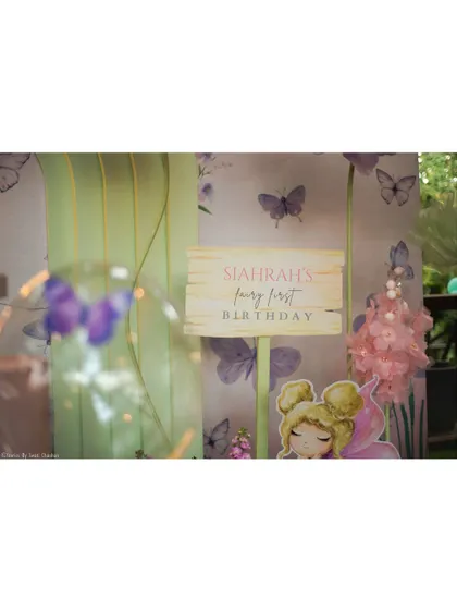 A close-up of the personalized sign and a fairy cutout from 'Siahrah's Fairy First Birthday', set against a dreamy butterfly-themed background.