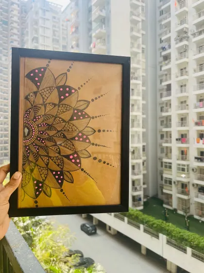 A semi-circle mandala on brown paper, framed and held up to show how it looks as wall decor.