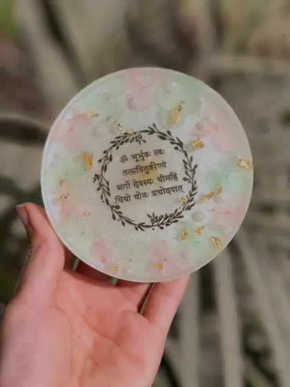 A beautiful coaster featuring the Gayatri Mantra, surrounded by a delicate floral wreath design. Perfect for your daily moment of peace.
