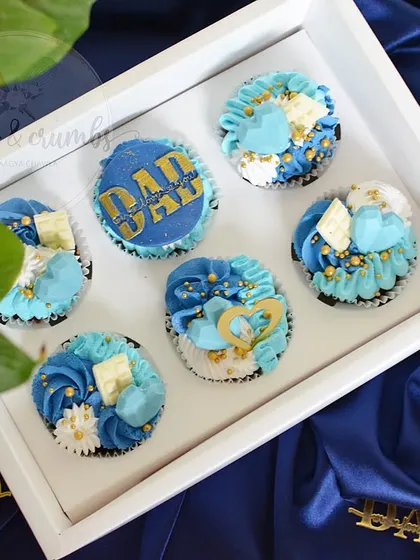 A full box of my special Father's Day cupcakes. The designs include a "DAD" topper and a mix of blue and white buttercream swirls with gold sprinkles.