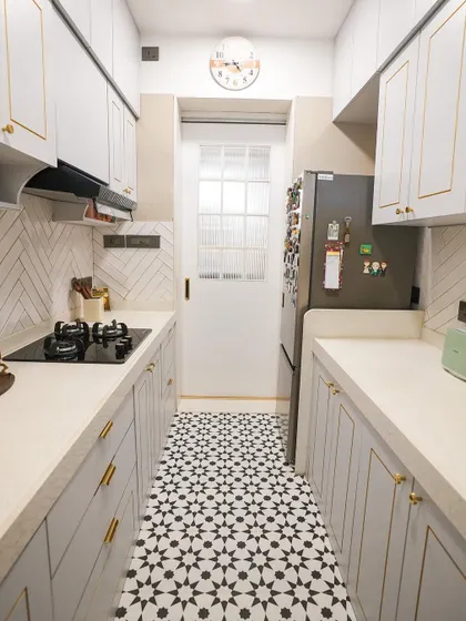 A minimalist black and white kitchen design. The patterned floor tiles add a bold graphic element, while the white cabinets with gold trim keep the space feeling bright and elegant.