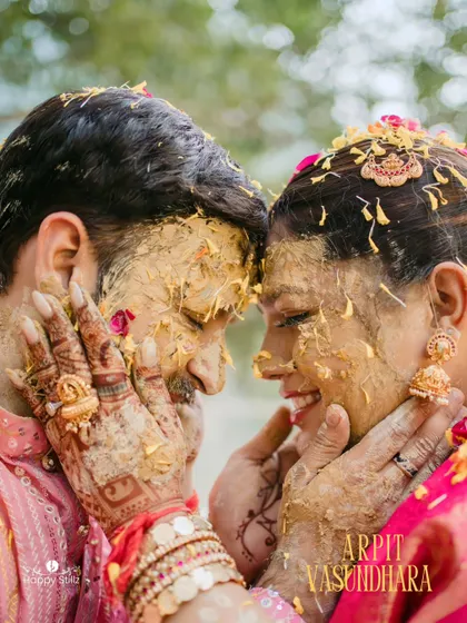 A beautiful, intimate close-up from a haldi ceremony. The bride lovingly applies turmeric to the groom, their faces close and covered in paste, capturing a moment of pure connection and joy.