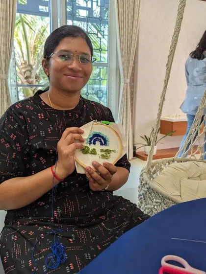 This participant is happy with her finished punch needle piece, featuring a serene rainbow and landscape design.