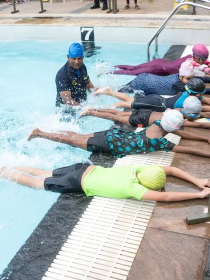 A coach guiding students through a kicking drill at the edge of the pool. This is how we build muscle memory for the correct swimming form.