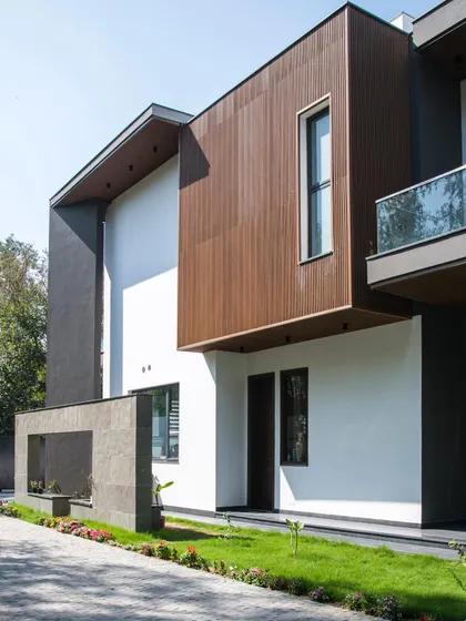 This view of Triveni Farmhouse highlights a projecting volume clad in rich brown wood, contrasting with the crisp white walls. This interplay of materials and forms is central to our goal of creating contemporary yet warm and inviting homes.