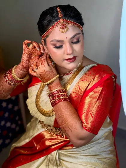 A candid moment of the bride putting on her earrings. This highlights the intricate details of her henna and the flawless, transfer-proof makeup that stays perfect throughout the ceremony.