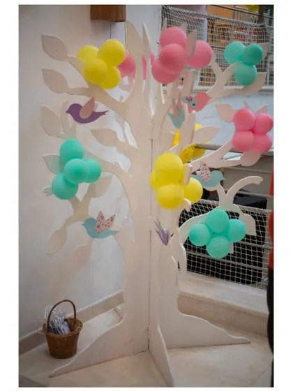 A stylized white tree prop decorated with small clusters of colorful balloons, a creative element from our birdhouse theme.